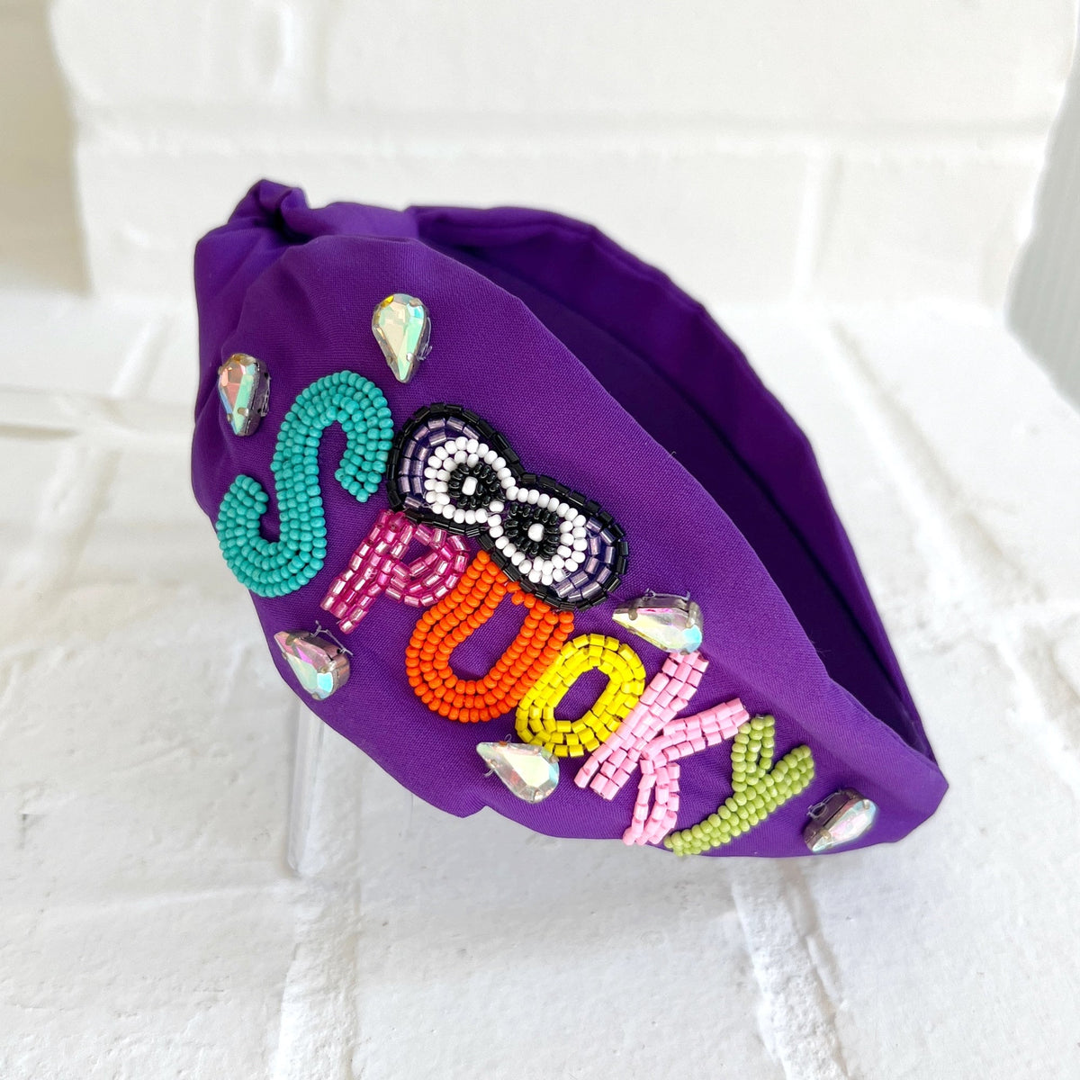 Purple knotted headband with multicolored SPOOKY beadwork, beaded eyes, and iridescent teardrop gems.